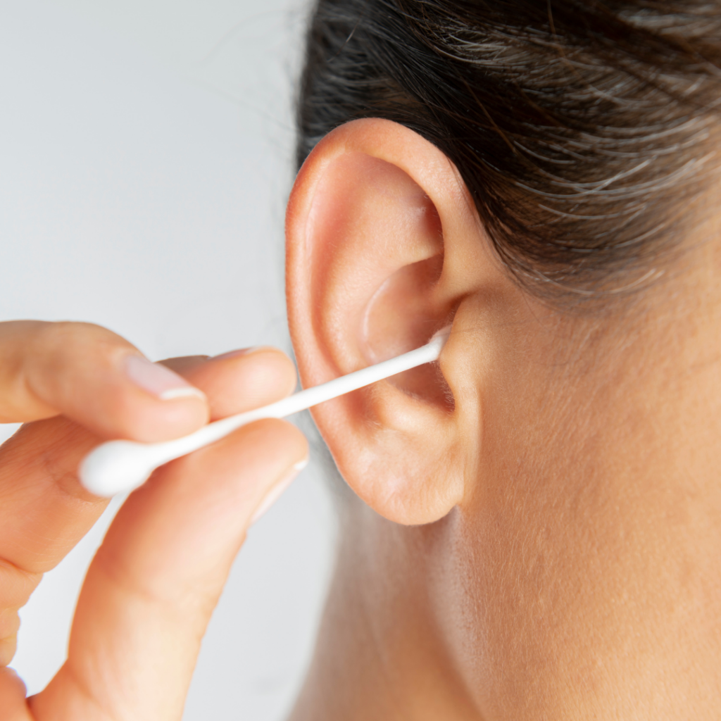 A person cleaning their ear with a cotton swab, close-up on the ear and hand.