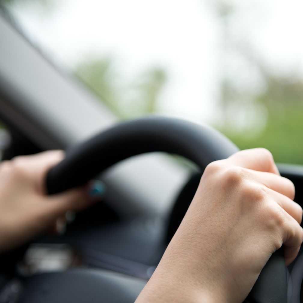 Hands gripping a car steering wheel from the drivers perspective.